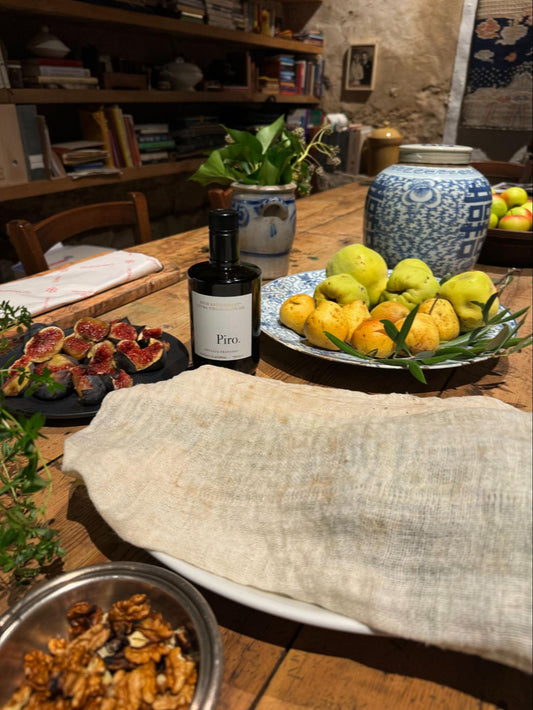 Rustic Mediterranean kitchen table with fresh figs, pears, walnuts, Olio Piro olive oil, and artisan ceramic jar
